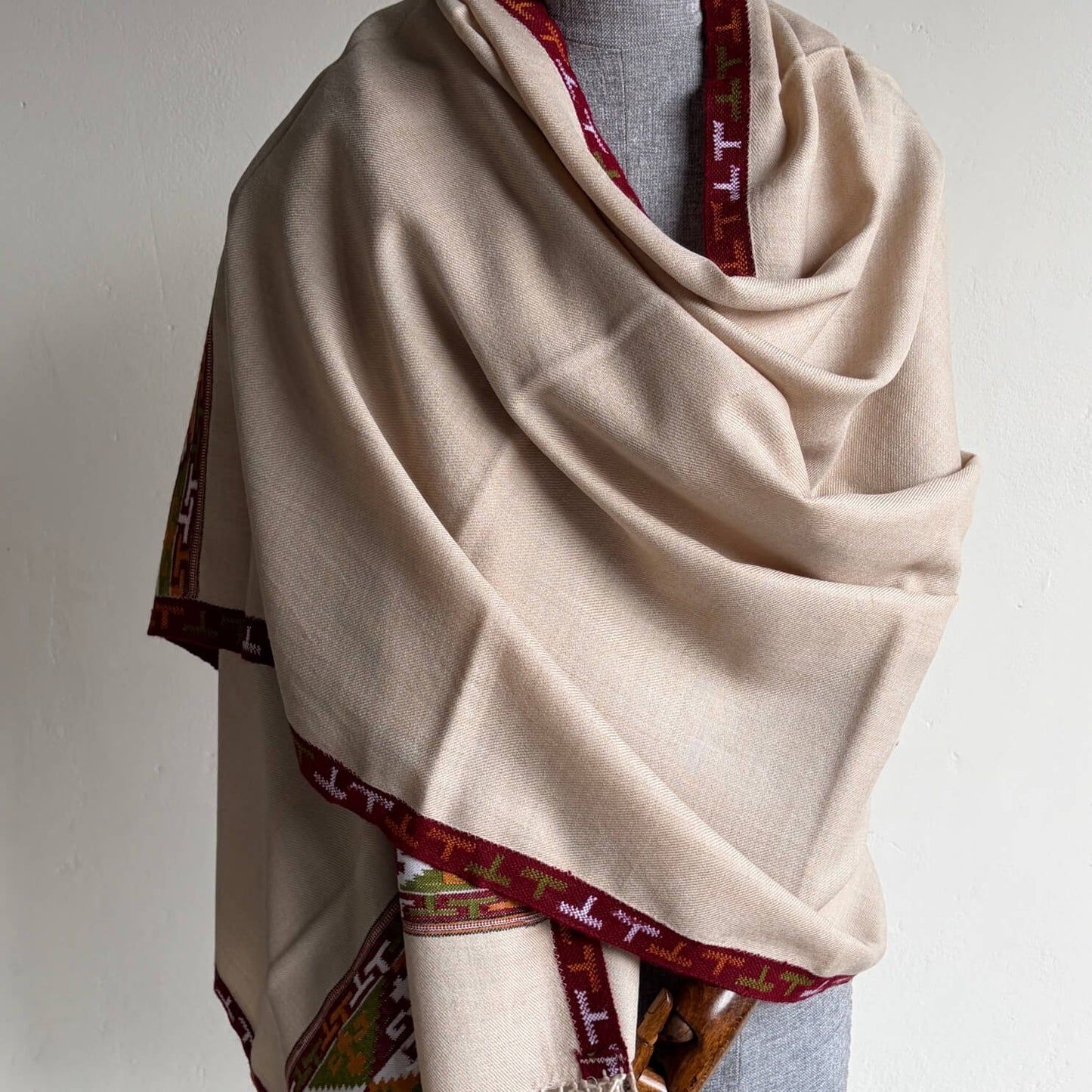 Beige Pure merino Kullu shawl with with red and green Kullu patti border draped over a mannequin against a white background