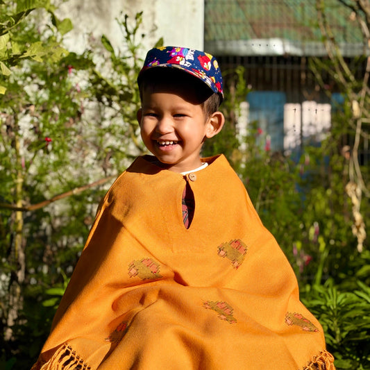 Child wearing a Sunshine Car Kids Poncho in mustard yellow in a garden setting